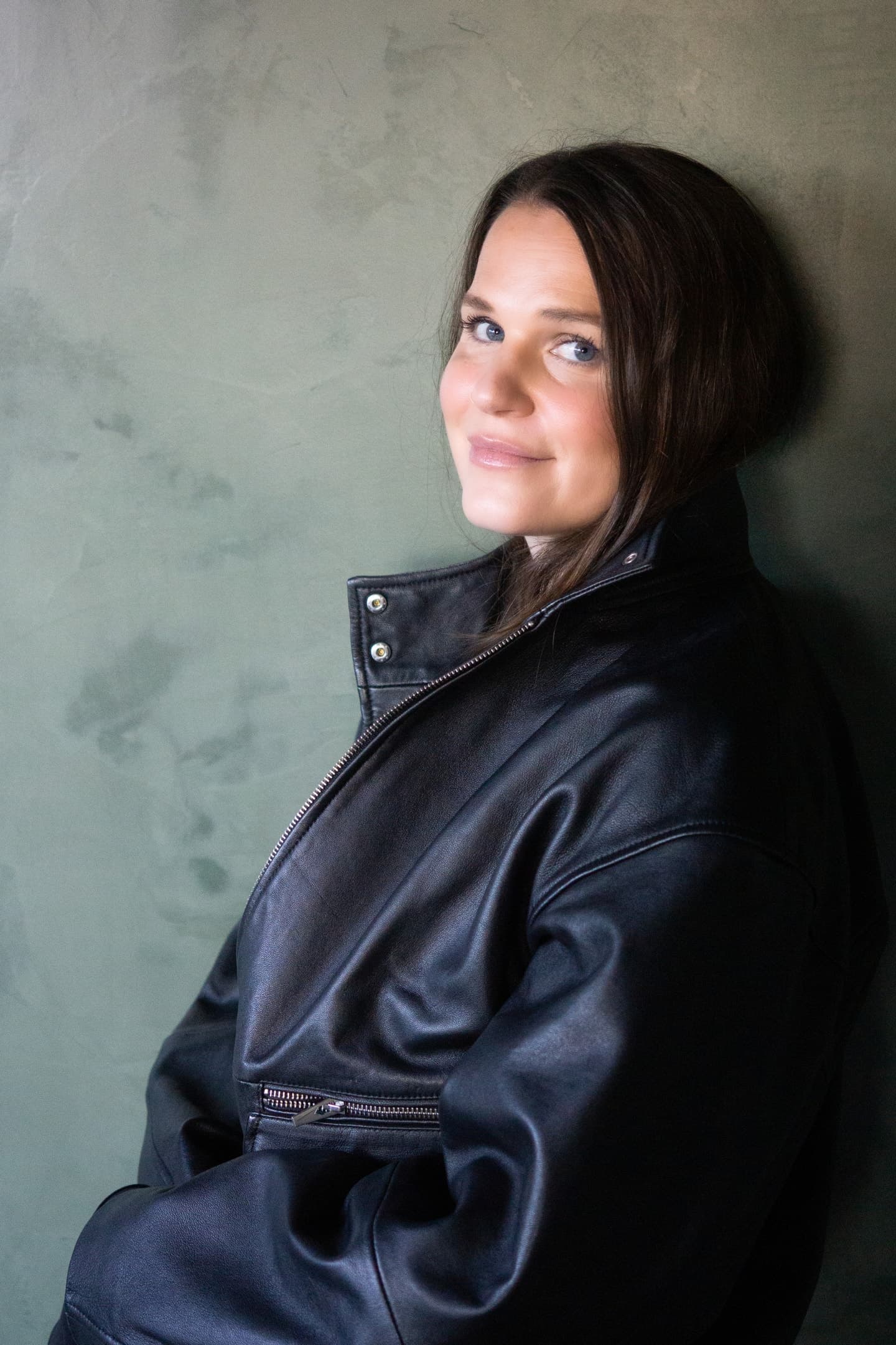 Liz Fryett seated in a dark jacket beside a softly lit wall.