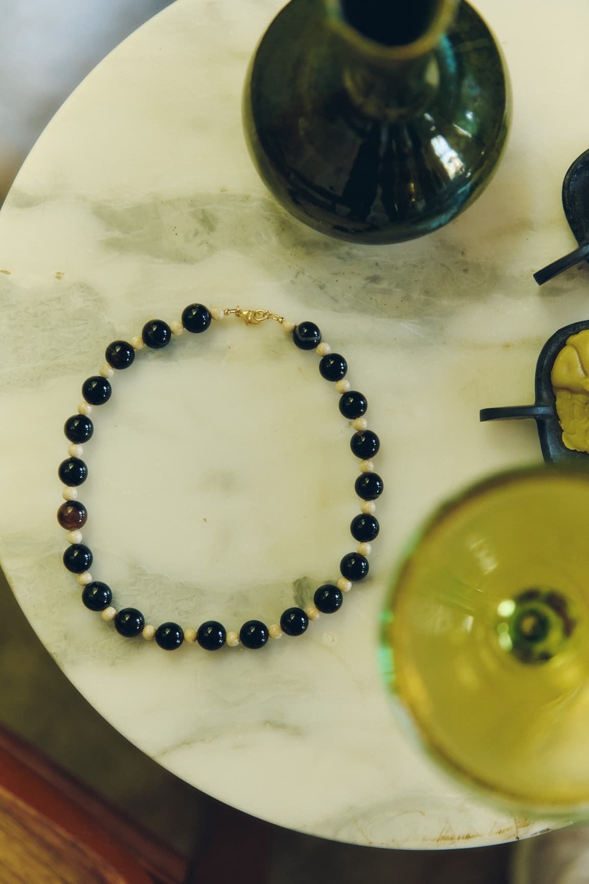 A beaded necklace arranged among green glassware on a sunlit table.